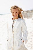 A young blonde woman on a beach wearing a white coat
