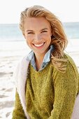 A young blonde woman by the sea wearing a knitted jumper and a denim shirt with another jumper over her shoulders