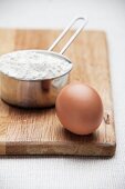 An egg and a saucepan of flour on a chopping board