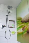 A hand-held shower head and a rain shower head on a white tiled wall with a partially visible printed glass back splash with a natural design in a shower