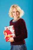 A young blonde woman holding presents and wearing a dark red jumper