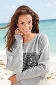 A young brunette woman by the sea wearing a grey sweatshirt