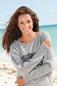 A young brunette woman by the sea wearing a grey sweatshirt