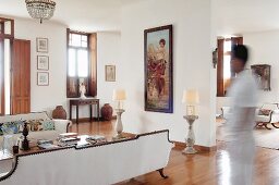Elegantes Foyer mit weisser Sofagarnitur, vor Raumteiler hochformatiges Bild zwischen Tischleuchten auf Steinstelen