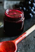 A jar of grape jam behind a used wooden spoon
