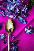 Dried hibiscus petals and an old spoon on a purple fabric napkin