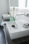 A square console basin on a double washstand with a dark wooden surface with water running from a square wall tap