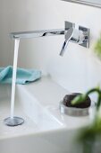 A strong jet of water coming from a wall tap into a square wash basin