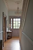 Chandelier hanging from stucco ceiling and staircase in pastel blue hallway of Victorian house