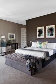 Elegantes Schlafzimmer in Brauntönen - gepolsterte Bank an Bettende des Doppelbettes, an dunkelbrauner Wand gerahmte Bilder