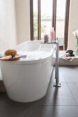 A free-standing bathtub in front of a balcony door with a floor tap on a slate floor