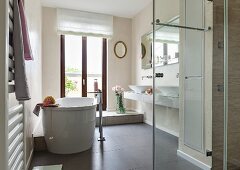Zeitgenössisches Badezimmer mit freistehender Badewanne vor Balkontür, im Vordergrund verglaster Duschbereich