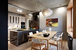 Wooden chairs with white-painted backrests around dining table and island counter in open-plan, loft-style kitchen