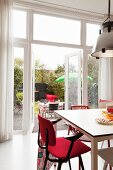 Red armchair at white table and open terrace doors in background