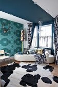 Wohnzimmer mit Mustermix: Tierfellteppich vor elegantem Sofa und drapierten Vorhängen, seitlich Geweihschädel auf floralem Tapetenmuster