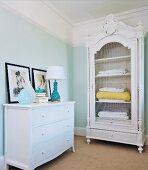 White chest of drawers and antique, white-painted, carved cupboard with wire door panel in corner of bedroom