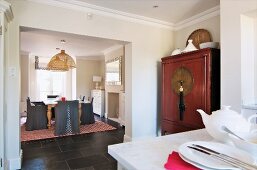 Kitchen with Oriental cupboard in niche; dining area with grey loose covers on chairs and tiled, country-house-style floor