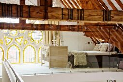 Bedroom on gallery behind glass screen with exposed wooden roof structure and Neogothic rose window with stained glass elements