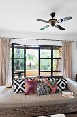 Deckenventilator über Sofa mit geometrisch gemusterten Kissen; geöffnete Fensterfront zu Terrasse im Hintergrund