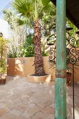 Grün patinierte, kunsthandwerklich verzierte Holzstütze auf mediterraner Terrasse mit Palmen