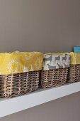 Detail of several baskets lined with patterned fabrics on white shelf on pale grey wall