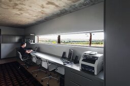 White office swivel chairs at long desk along one wall below ribbon window with view of landscape