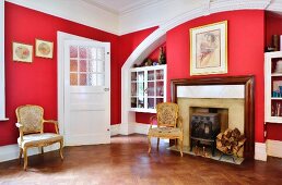 Masonry arch with integrated fireplace and fitted display cases and gilt, Rococo chairs in room with red walls