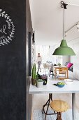 Pendant lamp with green metal lampshade above breakfast counter; woman in background next to dining area in open-plan interior