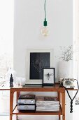 Wandtisch im Fifties Stil mit Vintage Telefon neben gerahmten Bildern, oberhalb minimalistische Vintage Pendelleuchte vor schmaler Wandscheibe