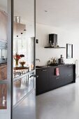 View through open door into kitchen with black base units and concrete floor