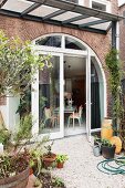 View from garden onto gravel terrace adjoining house with arched terrace doors and windows in brick facade