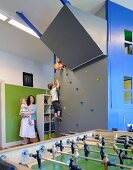 Mutter mit Kindern in Spielzimmer mit Kletterwand und Kicker im Vordergrund