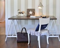 White wooden chair and simple table with wooden trestles against wall with striped wallpaper