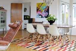 Retro dining area with woven, geometric rug and modern artwork on wall in background; leather armchair to one side