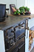 Old, cast iron cooker and plate of vegetables on top of masonry firewood store