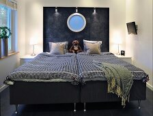 Dark grey double bed with striped cover, porthole with blue glass in charcoal-coloured headboard