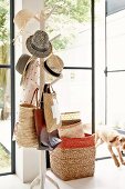 Collection of hats on tree-like coat stand, stacked baskets and open terrace door with view into garden