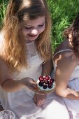 A girl wearing a white summer dress holding a fresh cherry tartlet