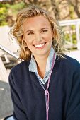 A young blonde woman outside wearing a dark blue knitted jumper and a denim shirt