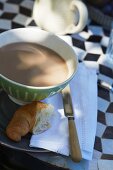 Cafe au lait and croissant on a bistro table with a black and white diamond pattern