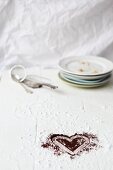 A cocoa powder heart, a stack of plates, a sieve and a cake slice on a floured work surface