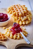 Frische Waffeln auf Holzbrett, eine mit Teelöffel Erdbeermarmelade