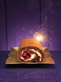 A chocolate Swiss roll with berries and a sparkler for Christmas