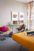 Pictures of viola flowers above narrow desk and 60s wicker chair and double bed with yellow bedspread in bedroom