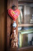 Key pendant with heart-shaped cushions and ribbon tassel hanging from key of glass-fronted cabinet