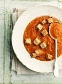 A bowl of tomato soup with croutons and a spoon