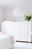 Pendant lamp with tulle lampshade and chest of drawers against pale, striped wallpaper in bedroom