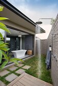 Garden shower on narrow patio with open, sliding glass doors leading into designer bathroom with free-standing bathtub
