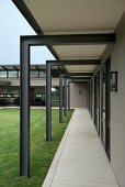 Open-sided arcade below steel structure leading along façade of architect-designed house