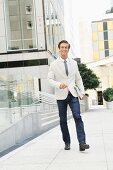 A young man wearing jeans, shirt, tie and a blazer in the road next to an office block